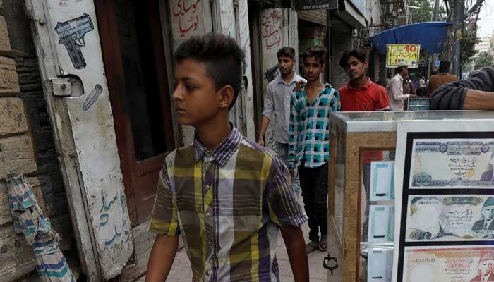 A boy walks past a sidewalk money exchange stall decorated with pictures of banknotes in Karachi. — Reuters/File