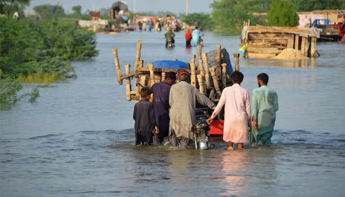 Men walk along a flooded road with their belongings, following rains and floods during the monsoon season in Sohbatpur, Pakistan August 28, 2022. — Reuters
