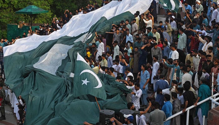 People carry a giant Pakistani flag while watching ´Beating the Retreat´ ceremony on the eve of the countrys Independence Day celebrations at the Pakistan-India Wagah border post, about 35km from Lahore on August 13, 2023.  — AFP