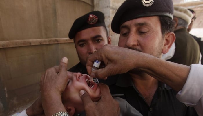 Health workers give polio vaccine drops to a child as police stand guard during a vaccination campaign in Peshawar, Khyber Pakhtunkhwa. — Reuters/File