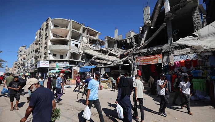 Palestinians walk past a destroyed building at a makeshift market in the Nuseirat refugee camp, located in the central Gaza Strip, on October 15, 2025. — Reuters