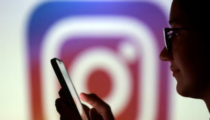A teenager poses for a photo while holding a smartphone in front of a Instagram logo in this illustration. — Reuters/File