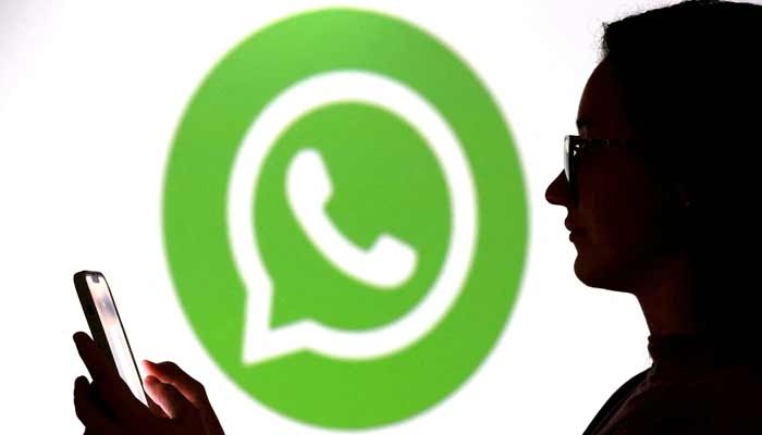Teenager poses for a photo while holding smartphones in front of a Whatsapp logo in this illustration taken September 11, 2025.— Reuters