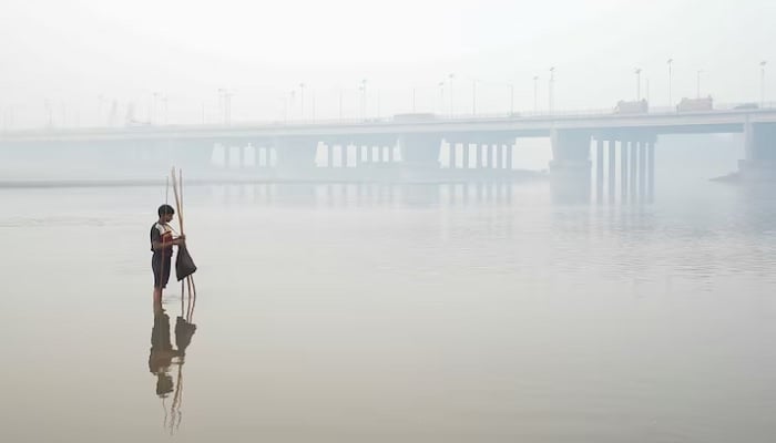 Faheem sets up a fishing trap, with the bridge over the River Ravi in the background, amid smog in Lahore, Pakistan, November 5. — Reuters