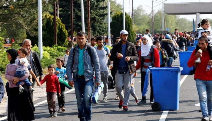 Migrants pass by garbage bins as they walk towards the Austrian border from Hegyeshalom, Hungary. — Reuters
