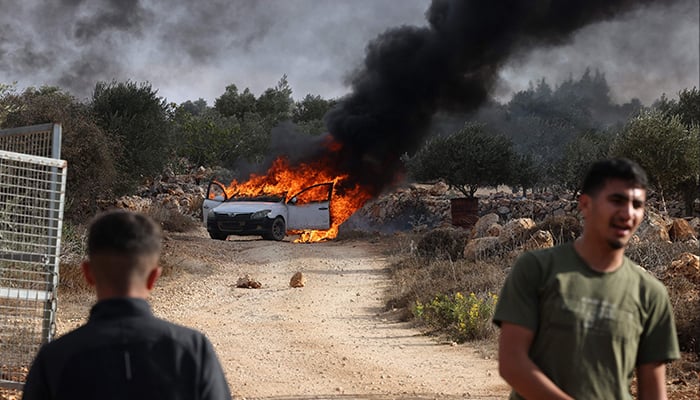 Palestinians stand near a burning car reportedly set alight by Israeli settlers attempting to disrupt them harvesting olives near the occupied West Bank village of Turmos Ayya near Ramallah on October 19, 2025. — AFP