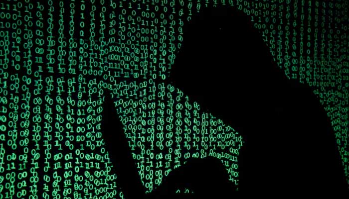 A hooded man holds a laptop computer as cyber code is projected on him in this illustration picture taken on May 13, 2017. — Reuters
