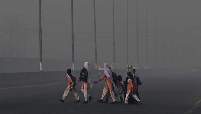 School children cross a road amid dense smog in Lahore on October 27, 2025. — AFP
