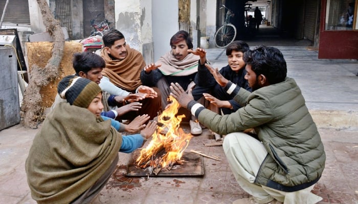 A group of youngsters sit around a bonfire to warm themselves on a chilly morning as temperatures drop during winter in Multan. — APP/File