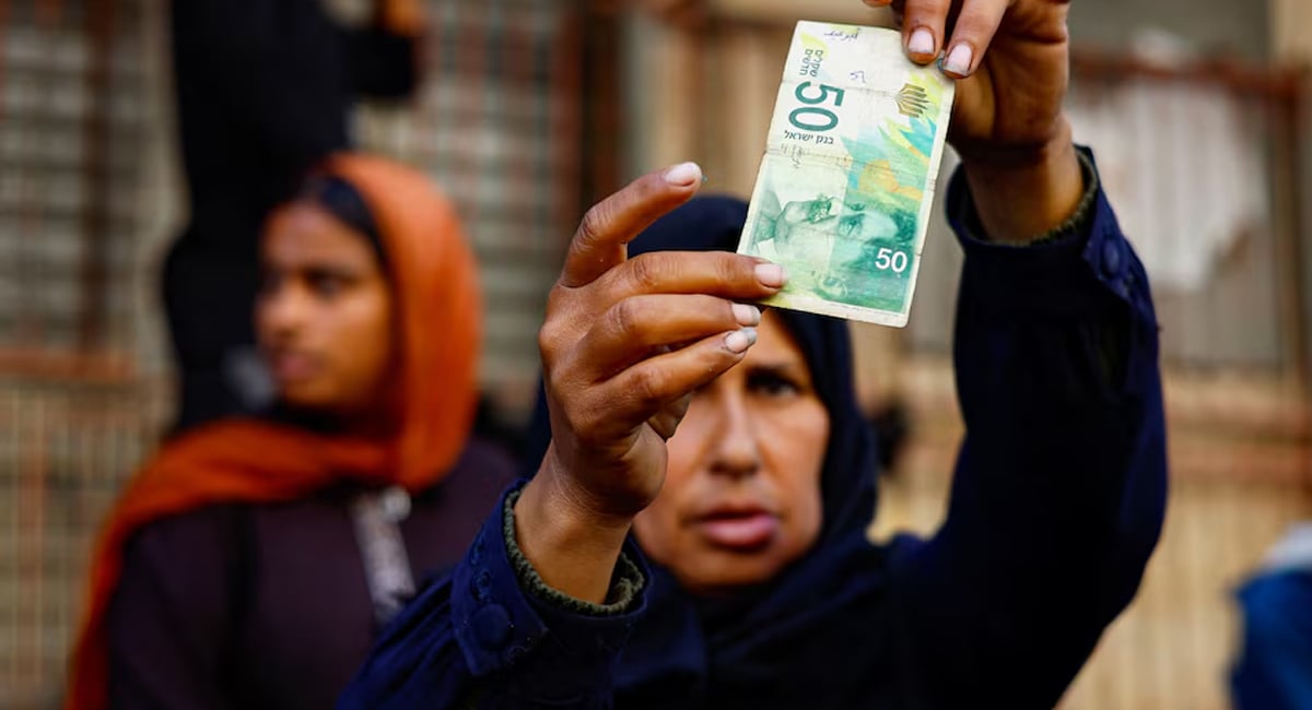Palestinian woman Manal al-Saidi examines a damaged banknote as she repairs money on a street, amid a cash crisis, in Nuseirat, central Gaza Strip, October 27, 2025. — Reuters