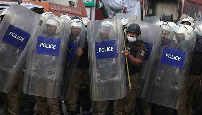 Police officers in riot gears stand guard behind the shield to avoid stones hurled by the supporters of PTI Chairman Imran Khan, during clashes ahead of his possible arrest outside his home, in Lahore, March 14, 2023. — Reuters