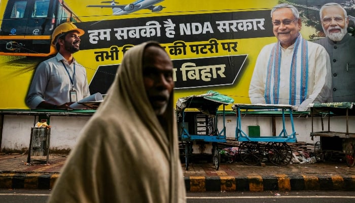 In this photograph taken on November 1, 2025, a man walks past a banner featuring Narendra Modi (R), India´s Prime Minister and leader of the Bharatiya Janata Party (BJP) and Nitish Kumar (2R), Chief Minister of Bihar state and leader and election candidate of the Janata Dal United (JDU) party, displayed along a street in Patna, India, ahead of the state assembly elections. — AFP
