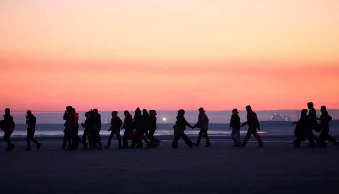 Migrants walk along the beach before trying to board an inflatable dinghy leaving the coast of northern France in an attempt to cross the English Channel to reach Britain.— Reuters