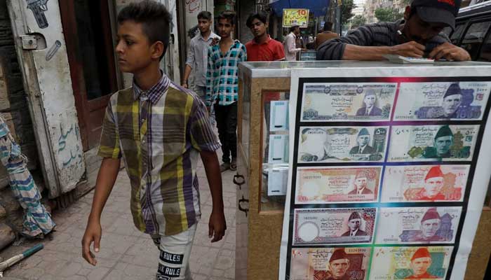 A boy walks past a sidewalk money exchange stall decorated with pictures of banknotes in Karachi. — Reuters/File