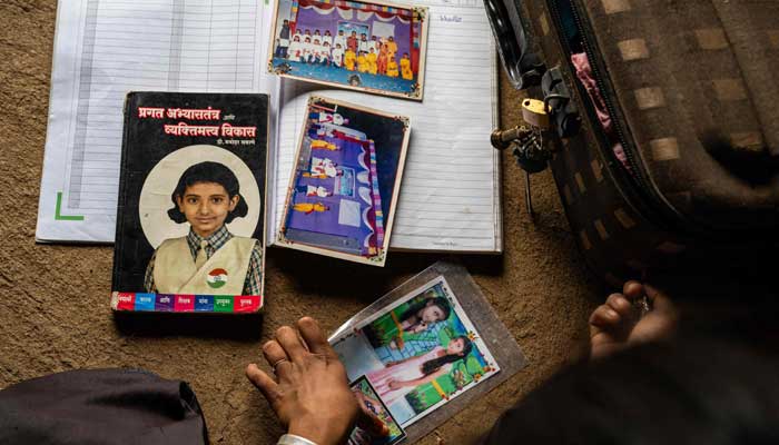 Ramati Mangla, who dropped out of school to manage household chores and fetch water, reminisces through her old school photographs and books inside her home at Bhadal village in the drought-prone district of Nandurbar on September 25, 2025. — AFP