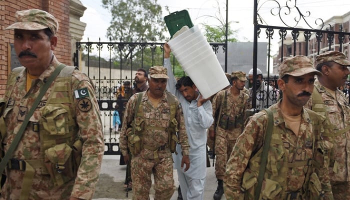 Pakistan Army soldiers walk alongside a presiding officer (centre) carrying ballot boxes as they come out from the voting materials distribution centre in Rawalpindi. — AFP/File