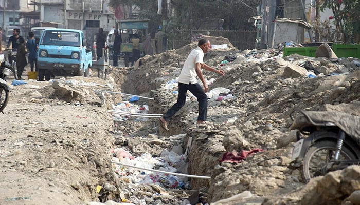 Commuters pass through a dug-up portion of a road in Karachi, on November 19, 2025. — Online