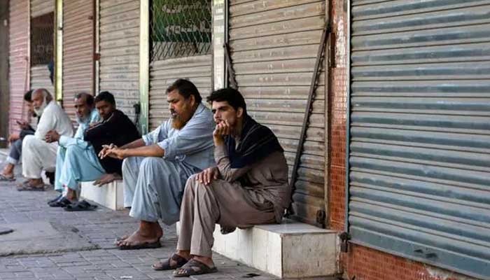 Men sit outside closed shops at a market. — Reuters/File