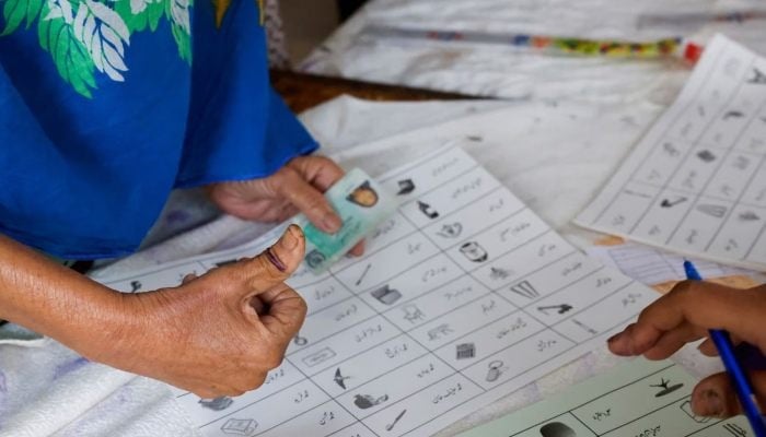 A voter with an ink mark on the thumb goes through paperwork to cast a vote during the general election in Karachi on February 8, 2024. — Reuters