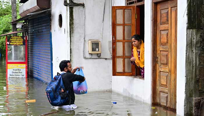 A man helps a woman stranded in a partially submerged house, at a flooded area in Wellampitiya on the outskirts of Colombo on November 29, 2025.— AFP