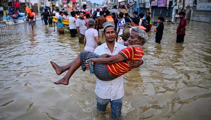 A youth carries an elderly man as they wade through a flooded street after heavy rainfall in Wellampitiya on the outskirts of Colombo on November 30, 2025.