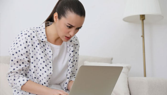 A representational image of a young woman looking anxious while working on her laptop. — Canva