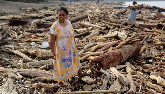 A woman stands amidst tree trunks that were stranded on a shore following deadly flash floods and landslides, in Padang, West Sumatra province, Indonesia on November 30, 2025. — Reuters