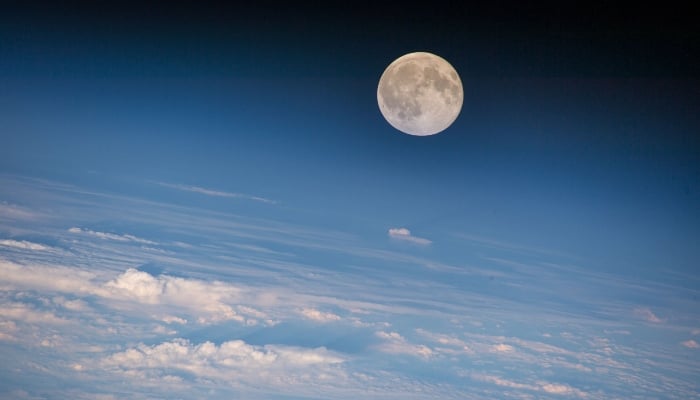 A full moon hangs above the blue glow of Earths atmosphere as white, fluffy clouds spread across the planet in this undated image. — X/@NASAAmes.