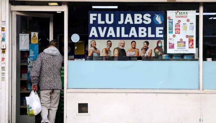 A man walks into a pharmacy with a sign advertising flu vaccinations, as hospitalisations rise, with Britain and other European countries grappling with a severe flu season and health authorities warning of increasing cases driven by a mutated strain of the virus, in London, Britain, December 11, 2025. —  Reuters