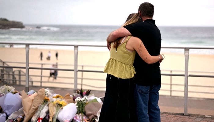 Mourners embrace near tributes piled together in memory of the victims of a shooting at Bondi Beach, in Sydney, on December 16, 2025. — AFP