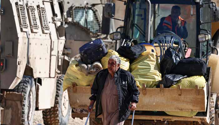 A man walks with crutches, followed by a bulldozer loaded with bags, as residents from the Nur Shams refugee camp return to their homes to retrieve belongings ahead of the Israeli military’s demolition of residential buildings in the camp near Tulkarem in the Israeli-occupied West Bank on December 17, 2025. — AFP
