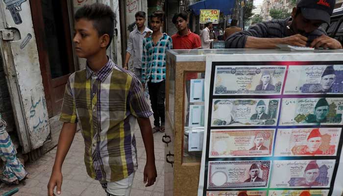 A boy walks past a sidewalk money exchange stall decorated with pictures of banknotes in Karachi on September 30, 2021. — Reuters