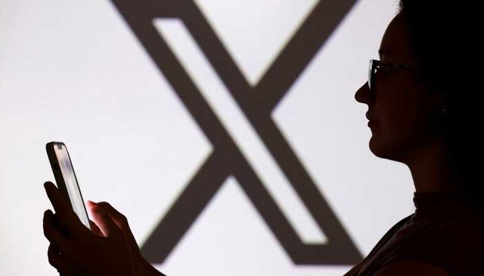 A teenager poses for a photo while holding a smartphone in front of a X logo in this illustration taken September 11, 2025. — Reuters