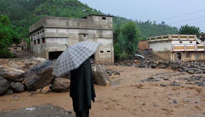 A resident stands with an umbrela as rain water flowing from mountains crosses a damaged area, following a storm that caused heavy rains and flooding in Bayshonai Kalay, in Buner district, in Khyber Pakhtunkhwa on August 18, 2025. — Reuters