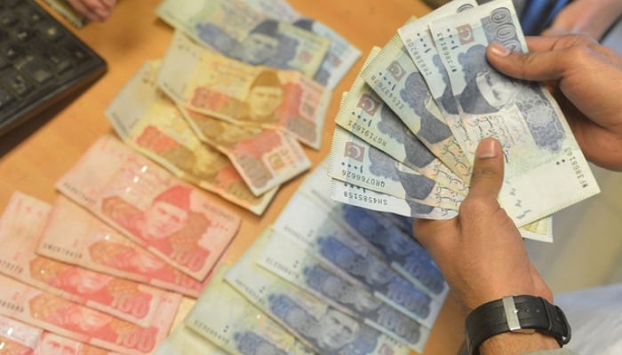 A money changer counts Pakistani currency at a market in Karachi. — AFP/File