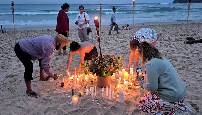 People light candles and lanterns on Manly Beach in Sydney on December 21, 2025. — AFP