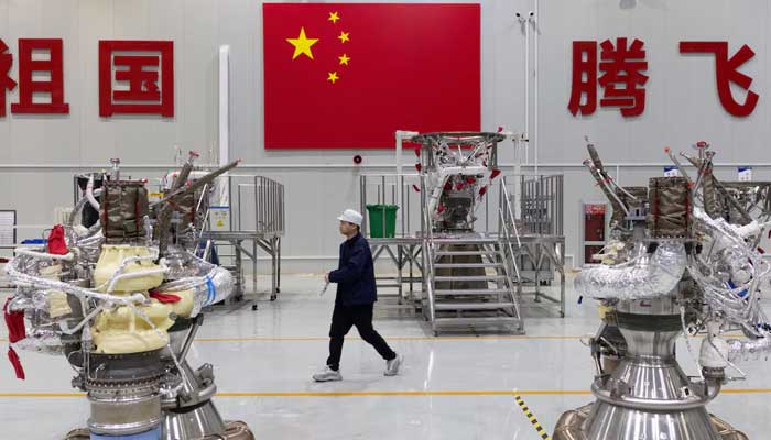 An employee walks next to rocket engines at the assembly hall with a national flag of China displayed in the background on the wall, at China’s private rocket company LandSpaces factory in Huzhou, Zhejiang province, China, December 17, 2025. — Reuters