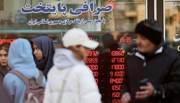 People walk past a display sign at a currency exchange bureau as the value of the Iranian rial drops, in Tehran, Iran, December 20, 2025.— Reuters