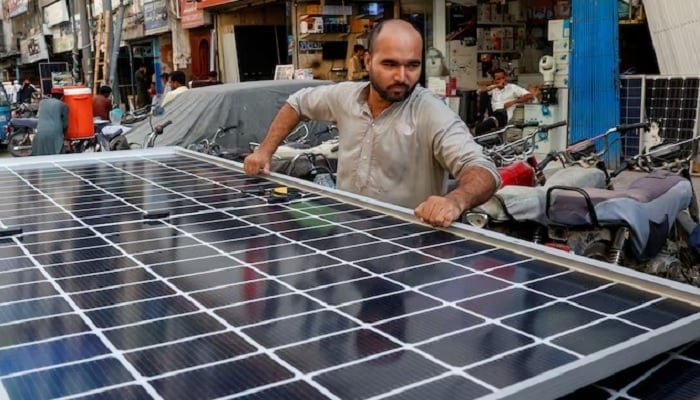 A worker loads solar panels on a vehicle, outside a shop at a market selling electronic items in Karachi, on June 11, 2024. —Reuters