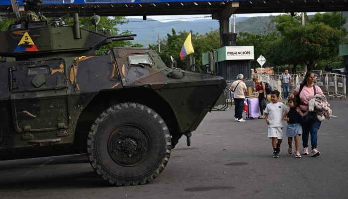 A woman with two kids walks past a military vehicle at the border crossing with Venezuela in Cucuta, Colombia, on January 3, 2026. — Reuters