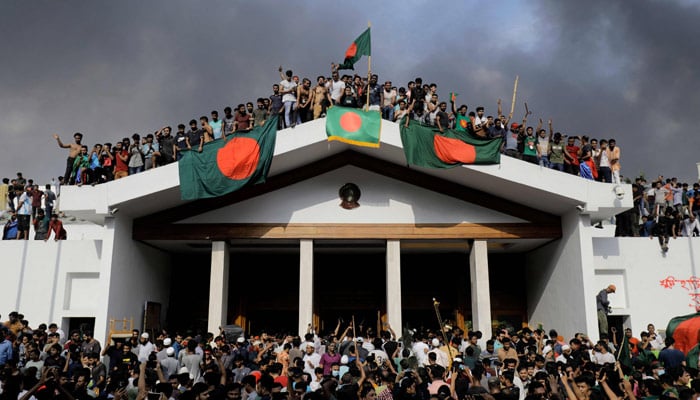 Anti-government protestors display Bangladeshs national flag as they storm Prime Minister Sheikh Hasinas palace in Dhaka on August 5, 2024. — AFP