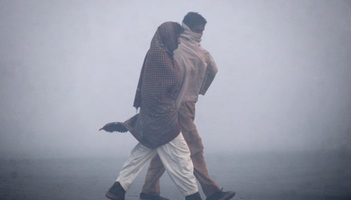 Men wrapped in warm shawls walk on a road on a chilly winter morning.  — Reuters