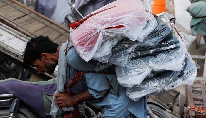 A labourer bends over as he carries packs of textile fabric on his back to deliver to a nearby shop in a market in Karachi. — Reuters/File
