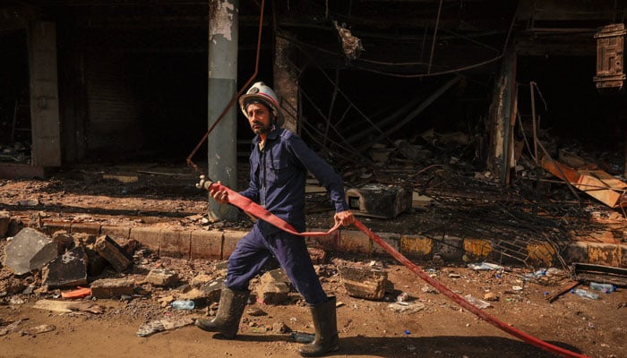 A firefighter pulls a water pipe at the site, following a massive fire that broke out in the Gul Plaza Shopping Mall in Karachi, January 20, 2026. — Reuters