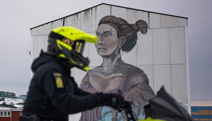 A police officer rides a snowmobile past a large mural depicting a woman and a polar bear on the side of an apartment building in Nuuk, Greenland, on January 21, 2026. — AFP