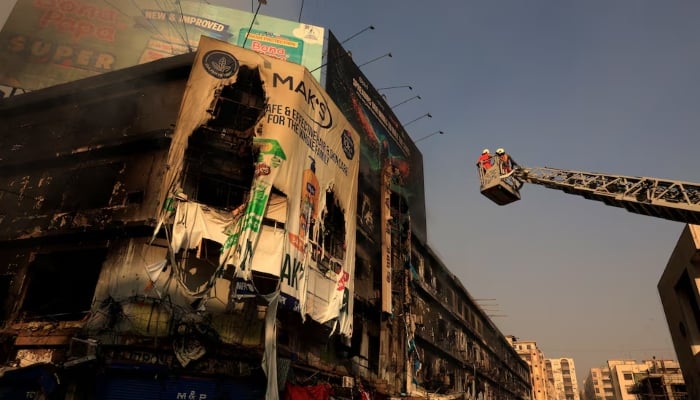 Firefighters work next to smoldering remains following a massive fire that broke out in the Gul Plaza in Karachi. — Reuters