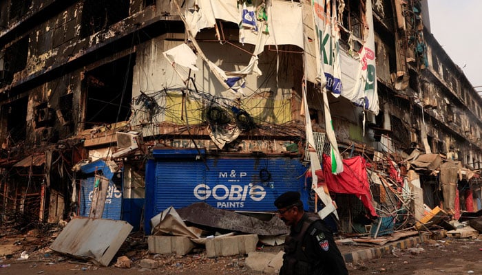 A police officer walks past a damaged building, following a massive fire that broke out in the Gul Plaza Shopping Mall in Karachi, January 22, 2026. — Reuters