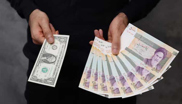 A currency dealer poses for a photo with a US one dollar bill and the amount being given when converting it into Iranian rials in an exchange shop in Tehran. — Reuters/File