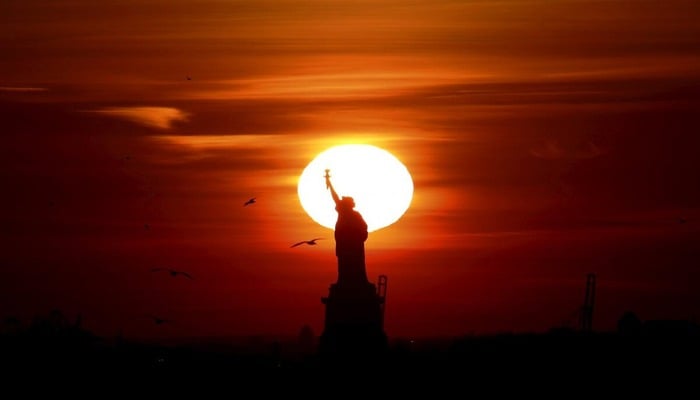 The sun sets behind the Statue of Liberty in New Yorks Harbor as seen from Brooklyn. — Reuters