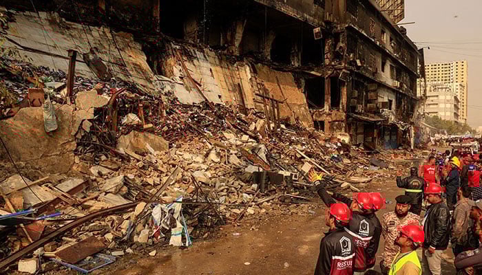 Fire department workers walk past the site, following a massive fire that broke out in the Gul Plaza shopping centre in Karachi on January 20, 2026. — Reuters